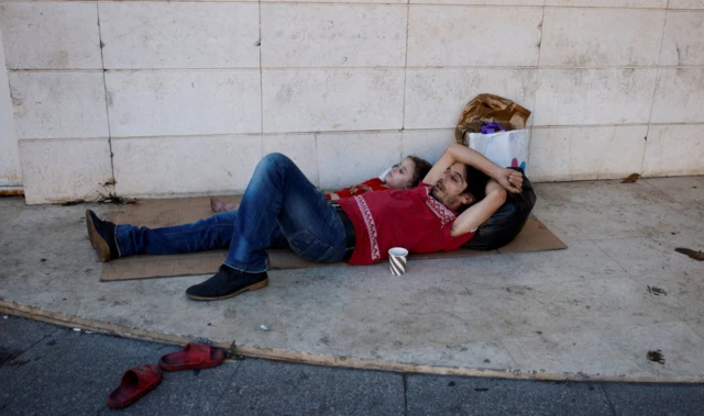 A man and a girl lie on a piece of cardboard next to a paper cup