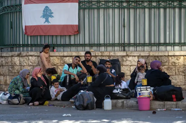 People rest on the sides of the streets with backpacks and belongings beside them