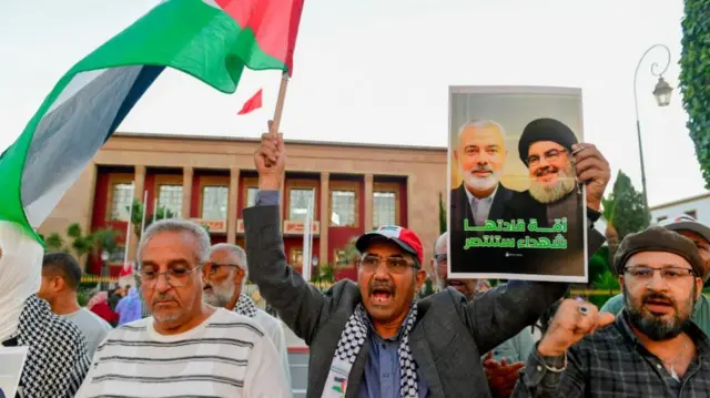 A group of men - one holding a poster featuring Nasrallah - take part in a protest following news of his death