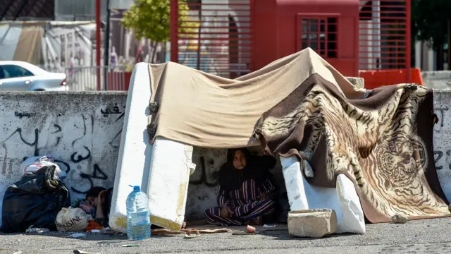 A woman shelters under a makeshift tent built with blankets and boulders