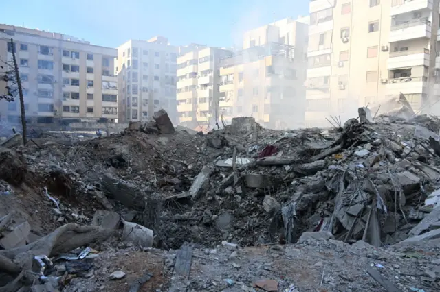 Rubble of flattened building with a backdrop of apartment blocks