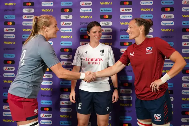 Captains Alex Matthews of England (L) and Kate Zackary of the United States (R) shake hands as they join Referee Aurelie Groizeleau