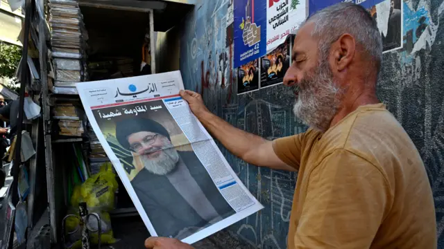 A man holding a newspaper featuring a picture of Nasrallah