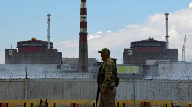 A serviceman with a Russian flag on his uniform stands guard near the Zaporizhzhia Nuclear Power Plant