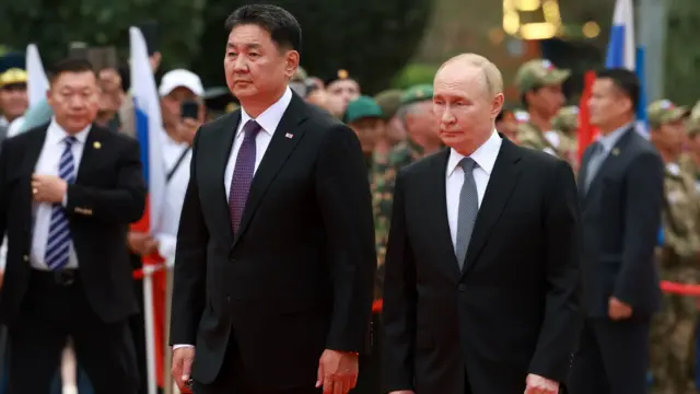 President Vladimir Putin and President Ukhnaagiin Khurelsukh walk along side-by-side, with military personnel in rows to the side