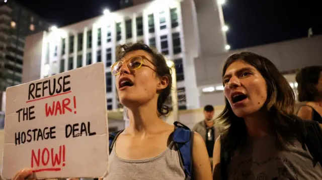 Two women protesting against goernment to show support for hostages holding sign saying 'refuse the war, hostage deal now'