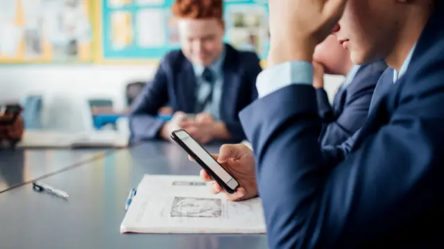 Pupils wearing a navy blazer holding mobile phones