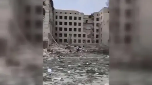 A multi-storey building surrounded by rubble with square holes with no glass windows in them and part of some floors destroyed