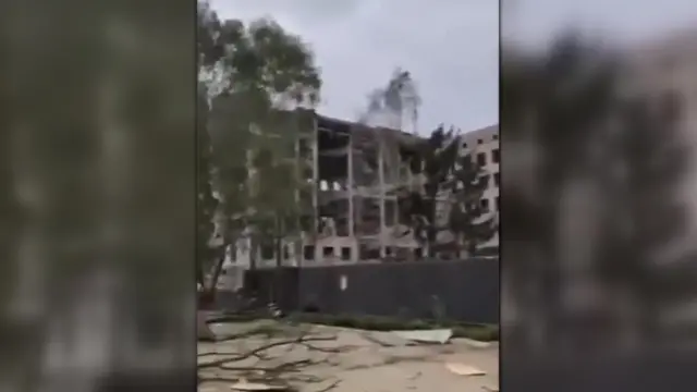 A building behind some trees with no glass windows and floors exposed to the outside