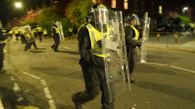 Police officers in protective gear carry riot shields