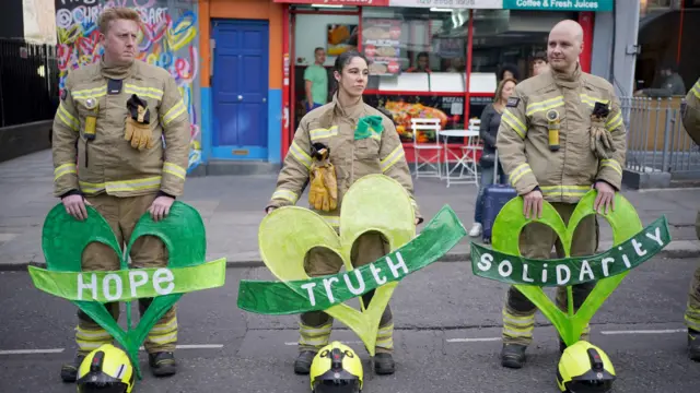 Firefighters form an honour guard, holding green hearts emblazoned with the words hope, truth and solidarity