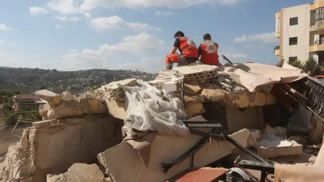 Two emergency workers sit on top a pile of rubble in Ain al-Delb, southern Lebanon