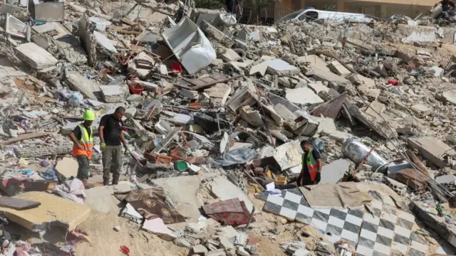 Three men stand in pile of rubble with lots of debris in aftermath of air strike in southern Lebanon