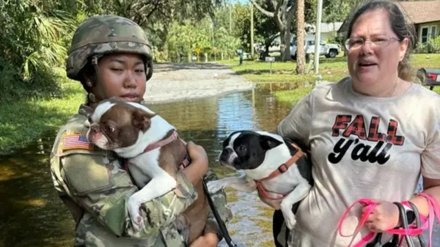 A troop hugs a dog in flood waters