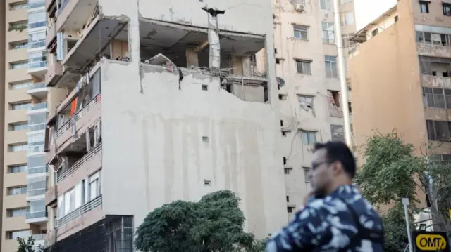 Man stands in front of tower damaged tower block in Kola, central Beirut