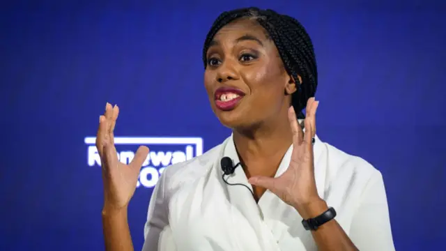 Kemi Badenoch addressing an audience in front of blue background