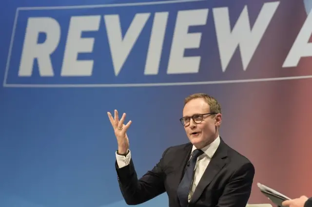 Tom Tugendhat with hand raised as he answers questions at conference in dark suit