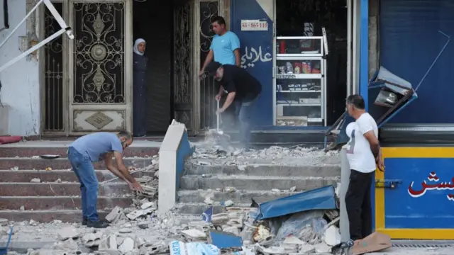 People clean up rubble outside building after air strike in Kola, Beirut