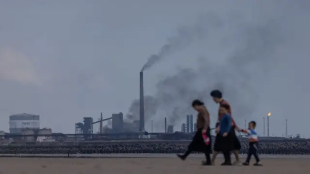 A family walk along Aberavon beach in view of the steel works in Port Talbot