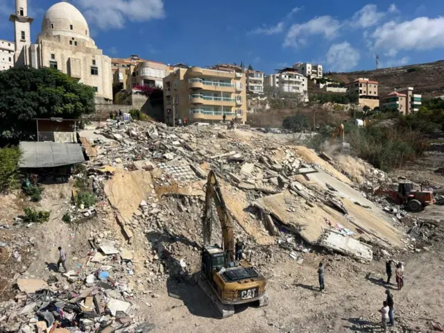 Excavator clearing rubble of flattened buildings