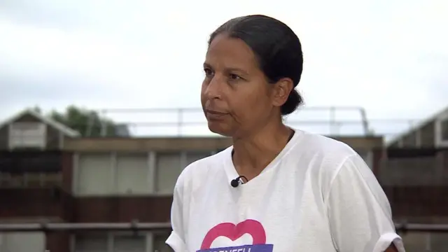 Lucy Masoud wearing a t-shirt with design that looks like the Transport for London logo but shaped like a heart with Grenfell written on it