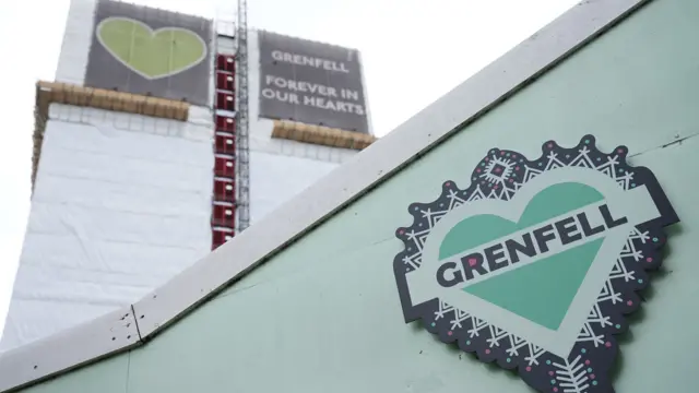 A shot looking up at the Grenfell tower featuring a sign at the top reading 'Grenfell - Forever in our hearts'