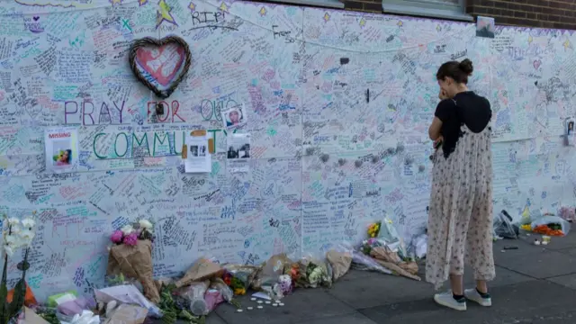 A woman stands at a wall with messages of condolence for Grenfell victims