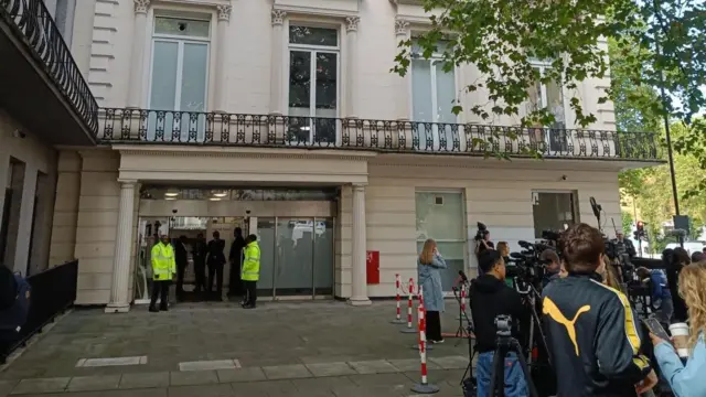 Two security members in hi vis at the entrance of Dorland House where a row of media cameras wait