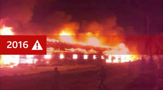 A picture of a burning school building at night, the image has a graphic with the date 2016 and a warning sign added to it