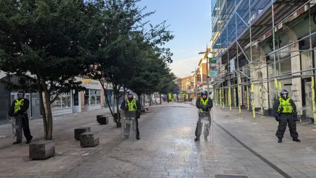 Security forces stand guard as riots erupt in Hull, Britain, August 3, 2024. The four security officers are dressed in riot gear and yellow reflective vests.