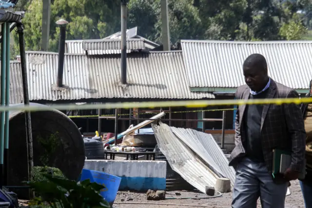 A man walks in front of police tape with the burnt out building behind him