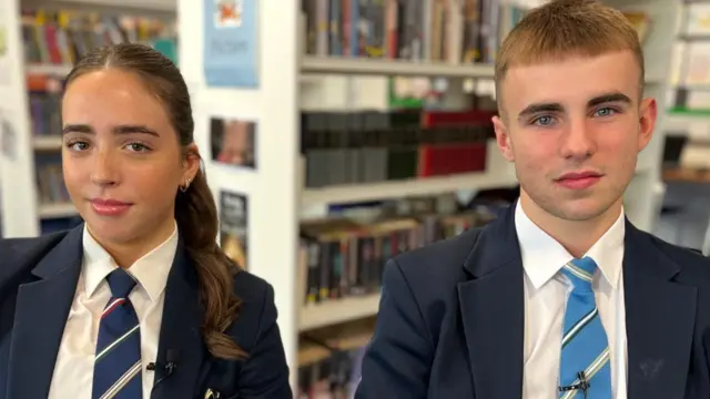 A girl wearing a uniform she has brown hair, she is with a boy wearing a uniform he has brown hair