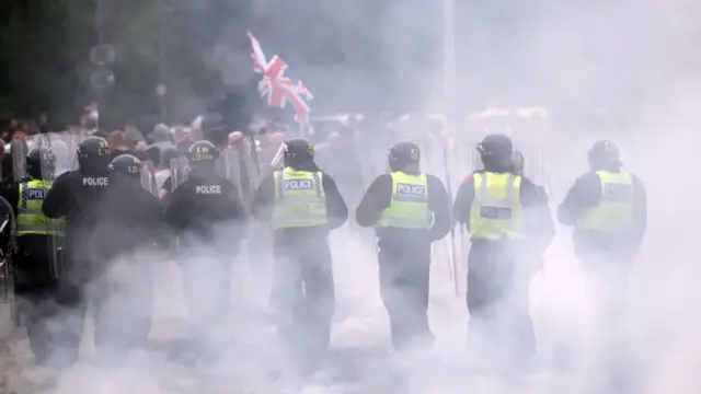 Riot police stand off against a crowd as smoke obscures the view