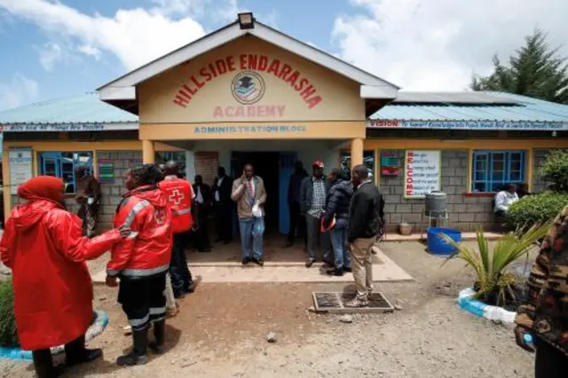 Red Cross volunteers stand in front of the entrance to the school alongside ordinary people