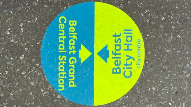 A green and blue sign that says - Belfast Grand Central Station and an arrow, then on the other side it says Belfast City Hall