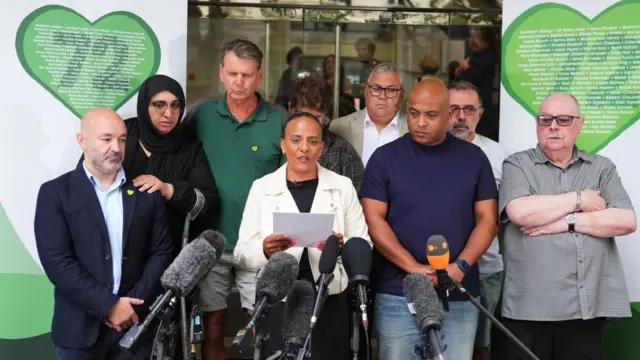 Members of the Grenfell United group address the media against banners with green hearts containing the names of the 72 victims of the fire