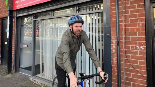 Gerry Carroll on a bike, he is wearing a green shirt and a blue helmet