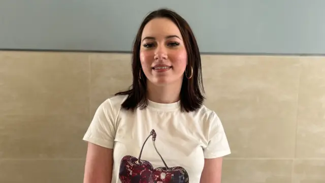 A woman wearing a white top, she has brown hair