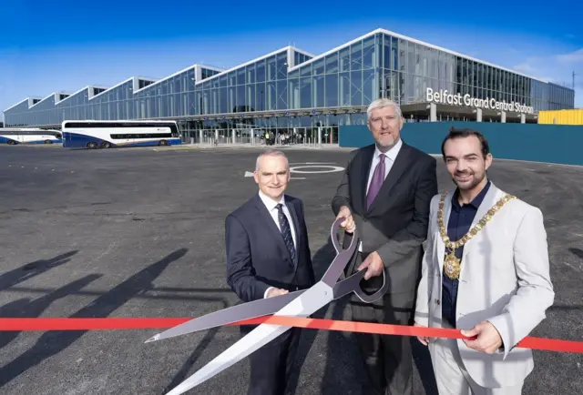 Three men in suits cutting the red ribbon outside the new Central Station.