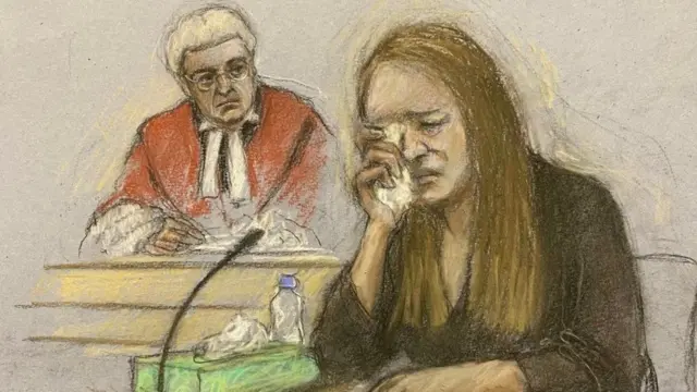 Court artist sketch of Lucy Letby's trial. She is sat in the dock in the foreground of the picture wearing all black, crying. Behind her sits the judge, in traditional judges clothing