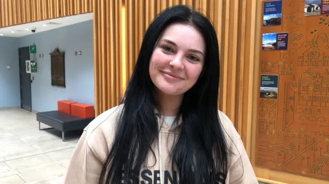 A woman with black hair and a cream top