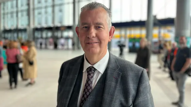 Edwin Poots standing in a grey suit