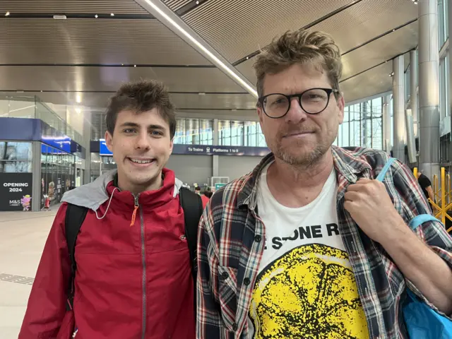Men in red coat and man in check coat standing in new station