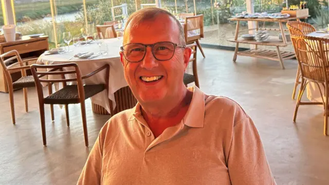 Paul Wickens, sitting in a restaurant, wearing a polo top with glasses
