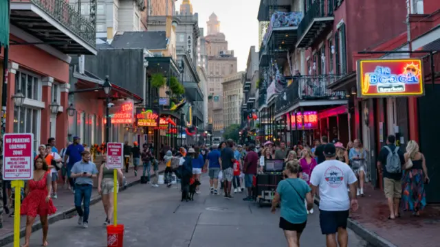 Bourbon Street full of pedestrians, with several neon signs indicating bars or restaurants.