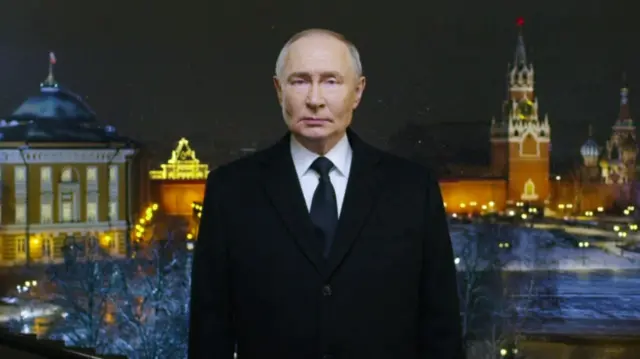 Vladimir Putin in a video message, wearing a black suit, tie and white shirt appears in front of a view of Russia at night.