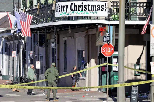 A yellow police cordon cordons off an area in New Orleans, below a banner attached to a building saying 'Merry Christmas!'