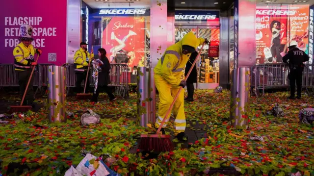 Three sanitation workers dressed in yellow sweep up confetti in front of a Skechers shop in Times Square in New York City.