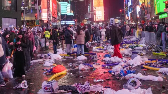 Garbage bags are seen scattered on the ground in Times Square as people mull about.