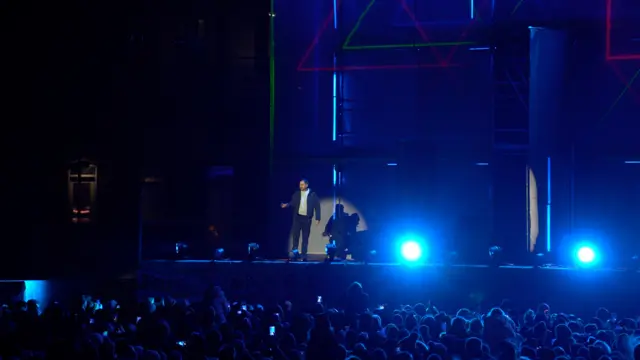 Man on large stage bathed in lights